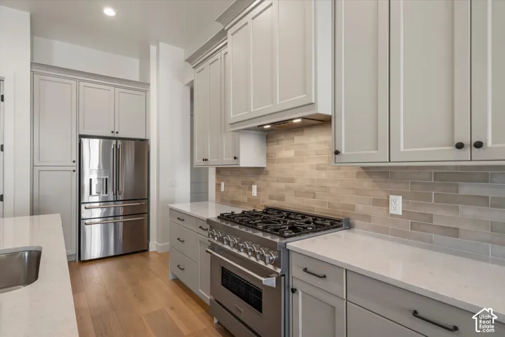 Stainless steel gas range, light wood-finish flooring, full-height tile backsplash, light-toned cabinetry, and an undermount sink