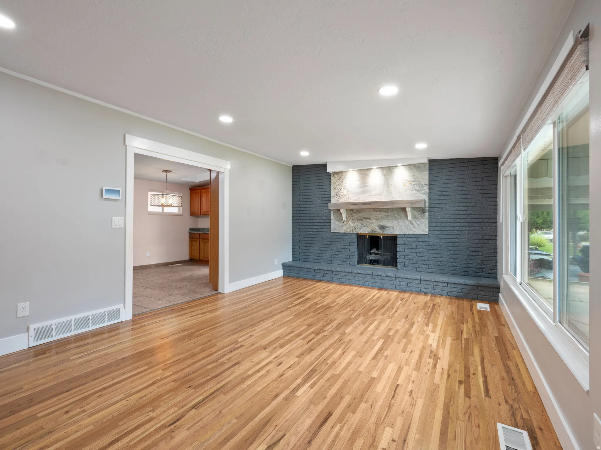 Unfurnished living room featuring a brick fireplace, light wood-type flooring, recessed lighting, brick wall, and an accent wall