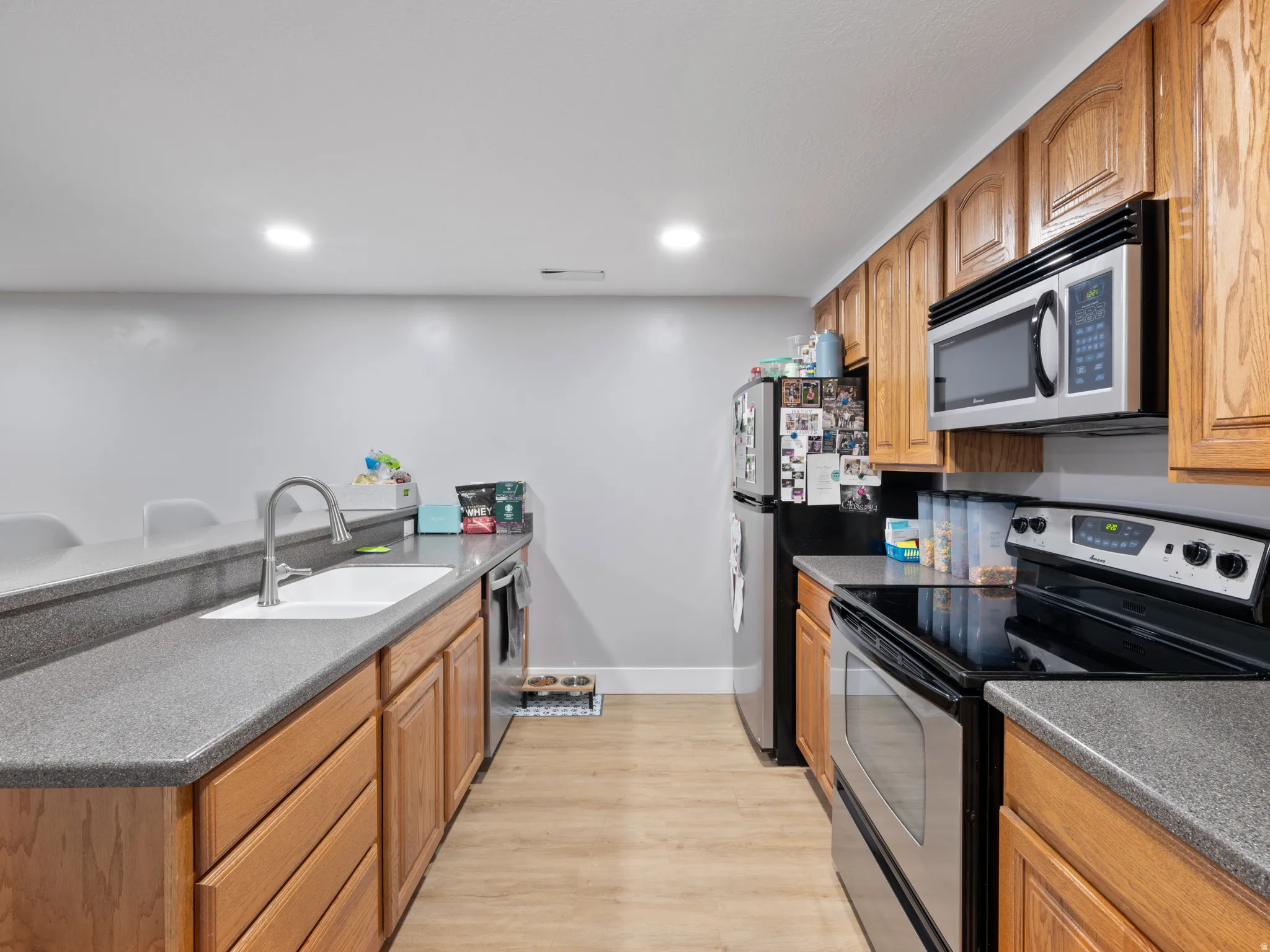 Kitchen with stainless steel appliances, a peninsula, wood finish cabinetry, light wood-type flooring, and recessed lighting