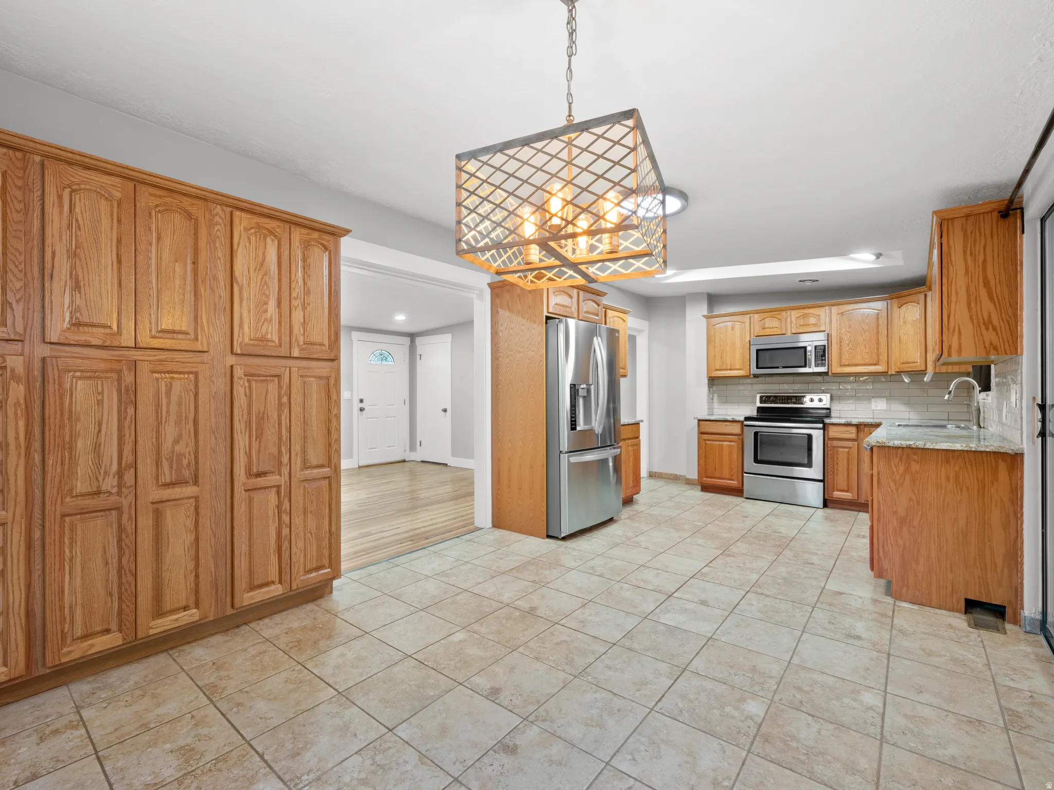 Kitchen with stainless steel appliances, decorative backsplash, light tile patterned floors, and decorative light fixtures