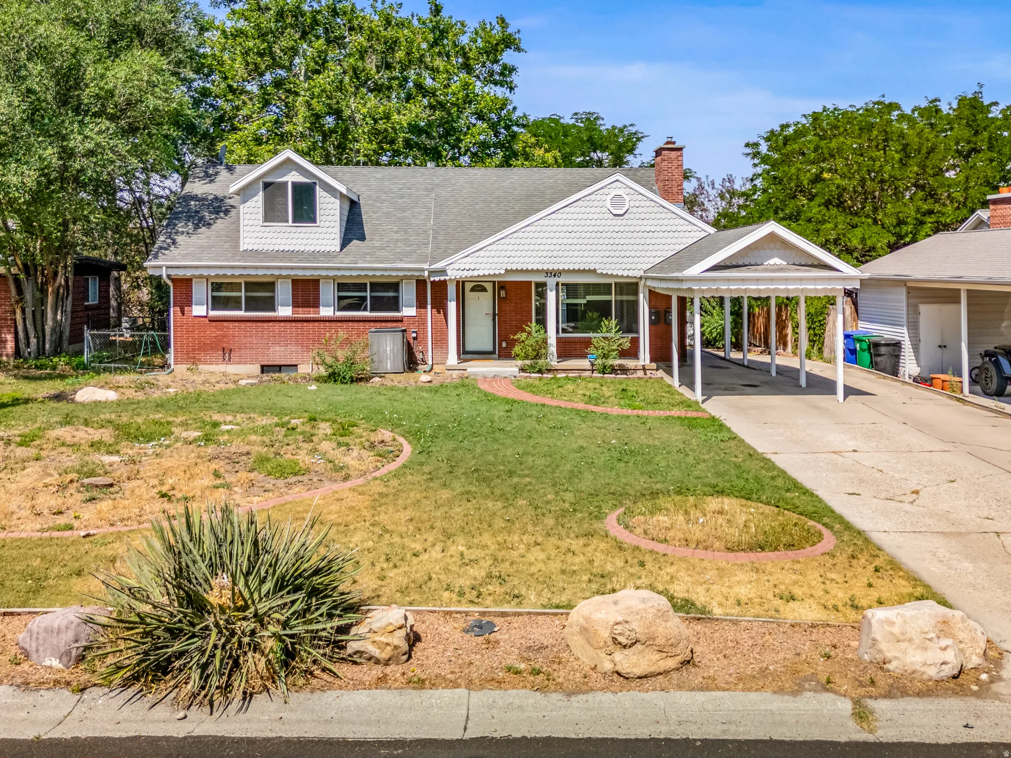 View of front of home featuring brick siding, concrete driveway, a carport, a chimney, and roof with shingles