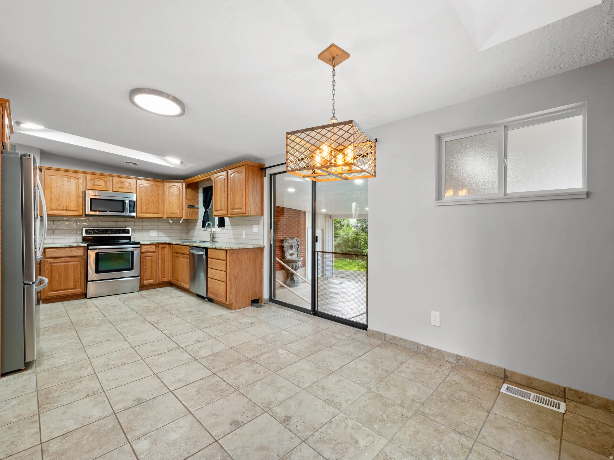 Kitchen with stainless steel appliances, tasteful backsplash, light tile patterned floors, and decorative light fixtures