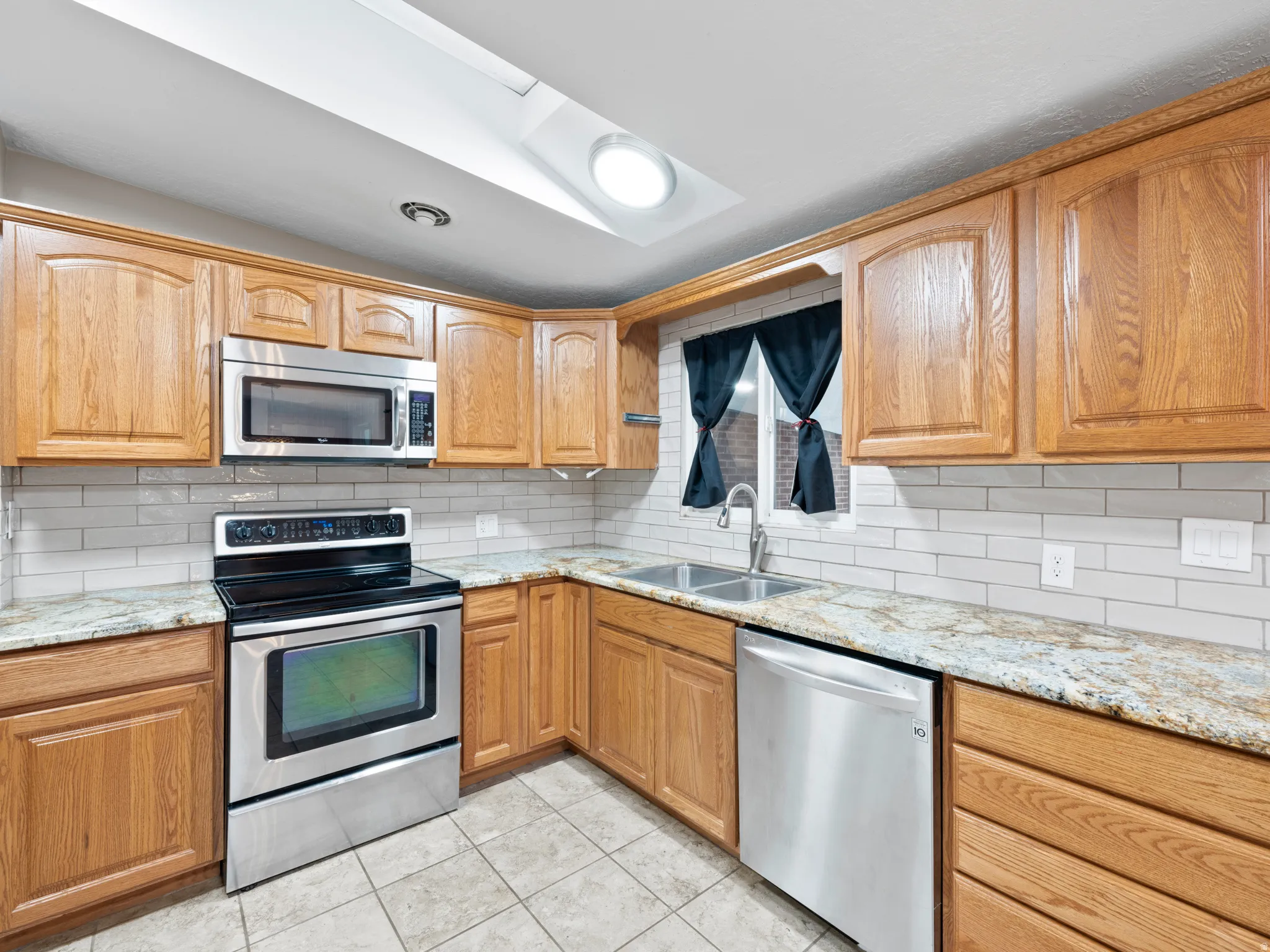 Kitchen with stainless steel appliances, light stone counters, backsplash, and light tile patterned flooring