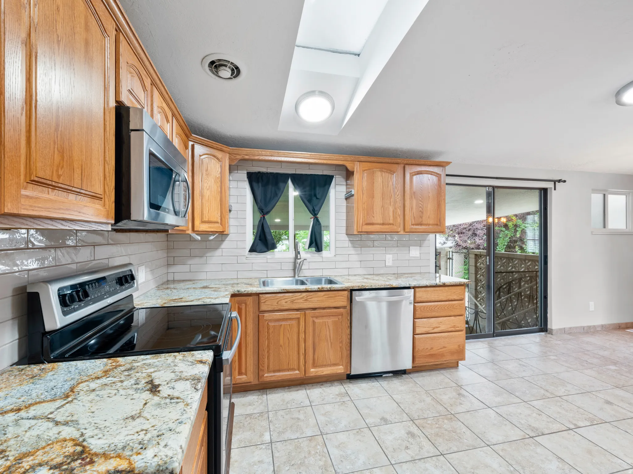 Kitchen featuring stainless steel appliances, light stone counters, decorative backsplash, and light tile patterned flooring
