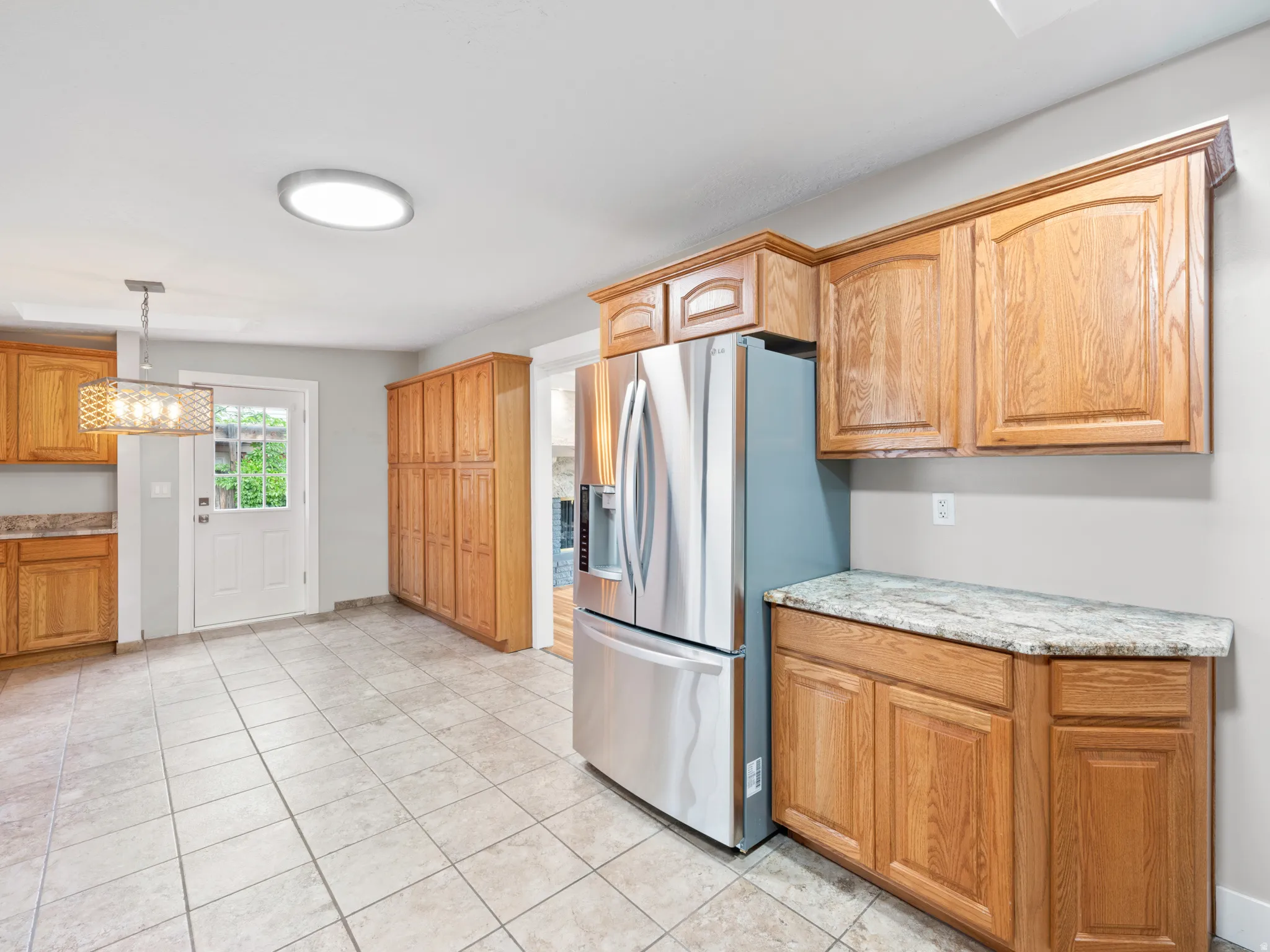 Kitchen featuring stainless steel fridge, hanging light fixtures, light tile patterned floors, and light stone countertops
