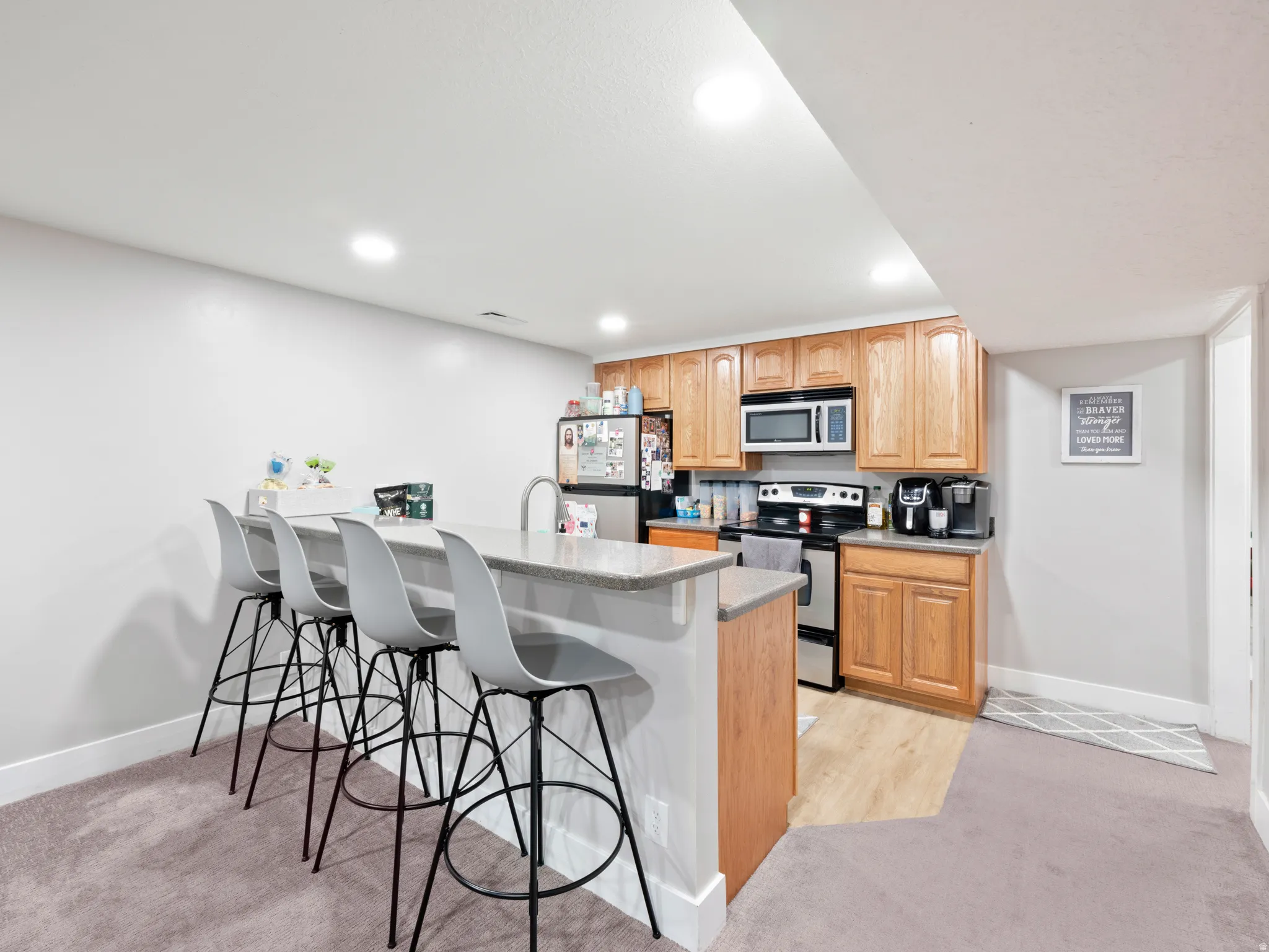 Kitchen featuring a breakfast bar area, stainless steel appliances, light carpet, a peninsula, and recessed lighting