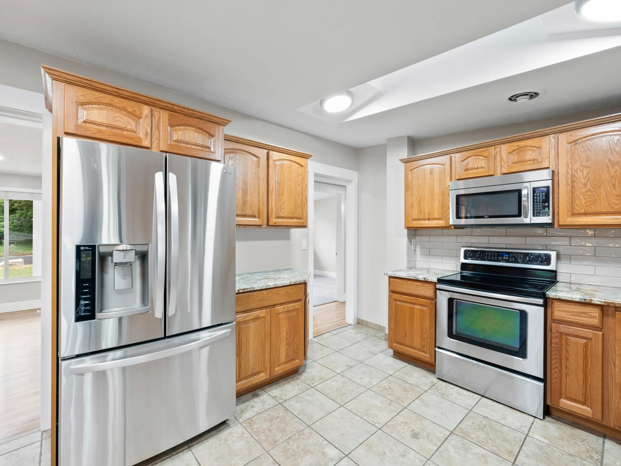 Kitchen featuring stainless steel appliances, light stone countertops, backsplash, recessed lighting, and light tile patterned floors