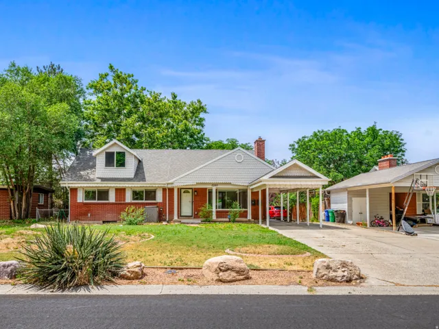 View of front facade with brick siding, driveway, a front lawn, a carport, and a porch