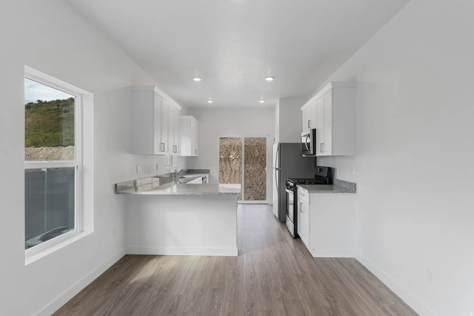 Kitchen featuring light stone countertops, white cabinets, gas stove, a peninsula, and light wood finished floors