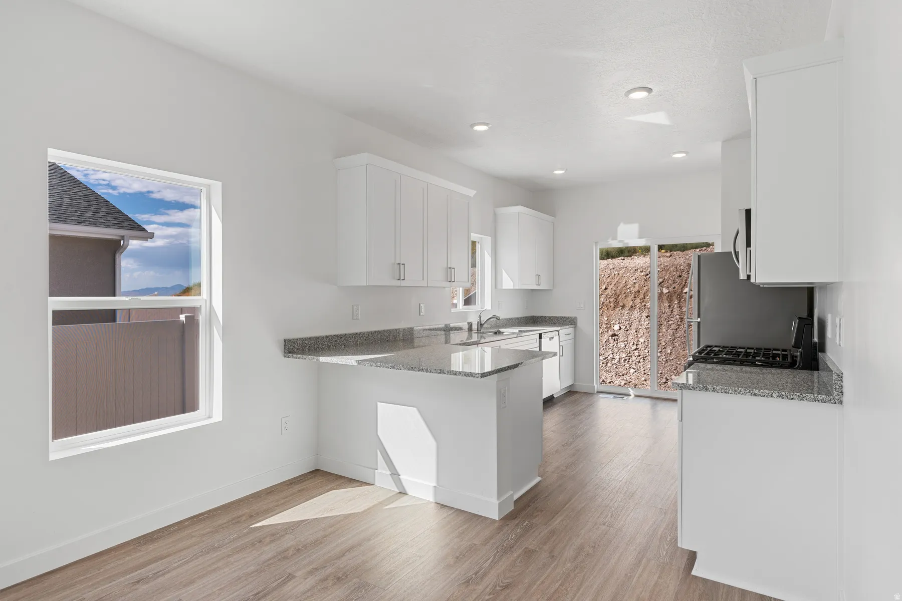Kitchen featuring white cabinets, light stone counters, a peninsula, light wood-style floors, and gas range