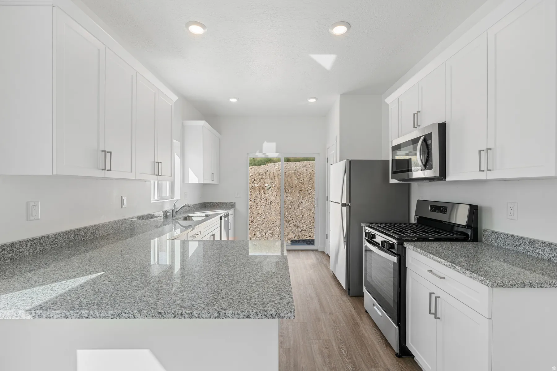 Kitchen featuring white cabinetry, stainless steel appliances, light stone counters, light wood-style floors, and recessed lighting