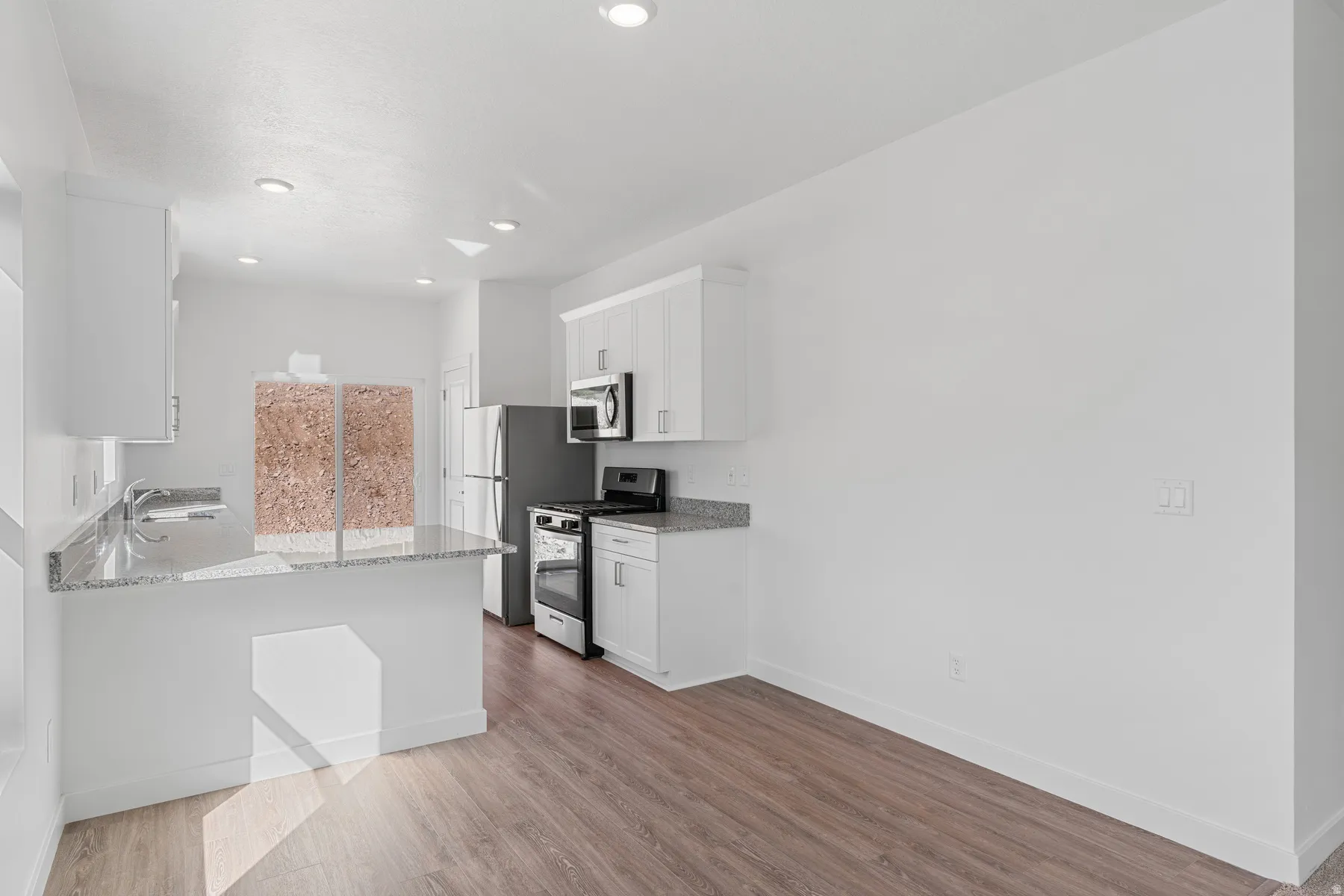 Kitchen with white cabinetry, light stone counters, stainless steel appliances, light wood finished floors, and a peninsula
