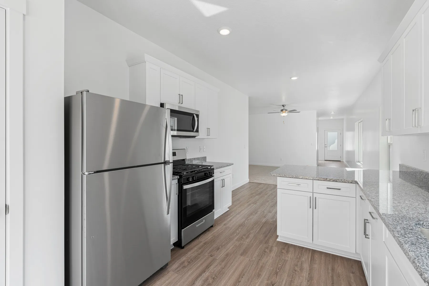 Kitchen featuring stainless steel appliances, white cabinets, light stone counters, light wood-style flooring, and a peninsula