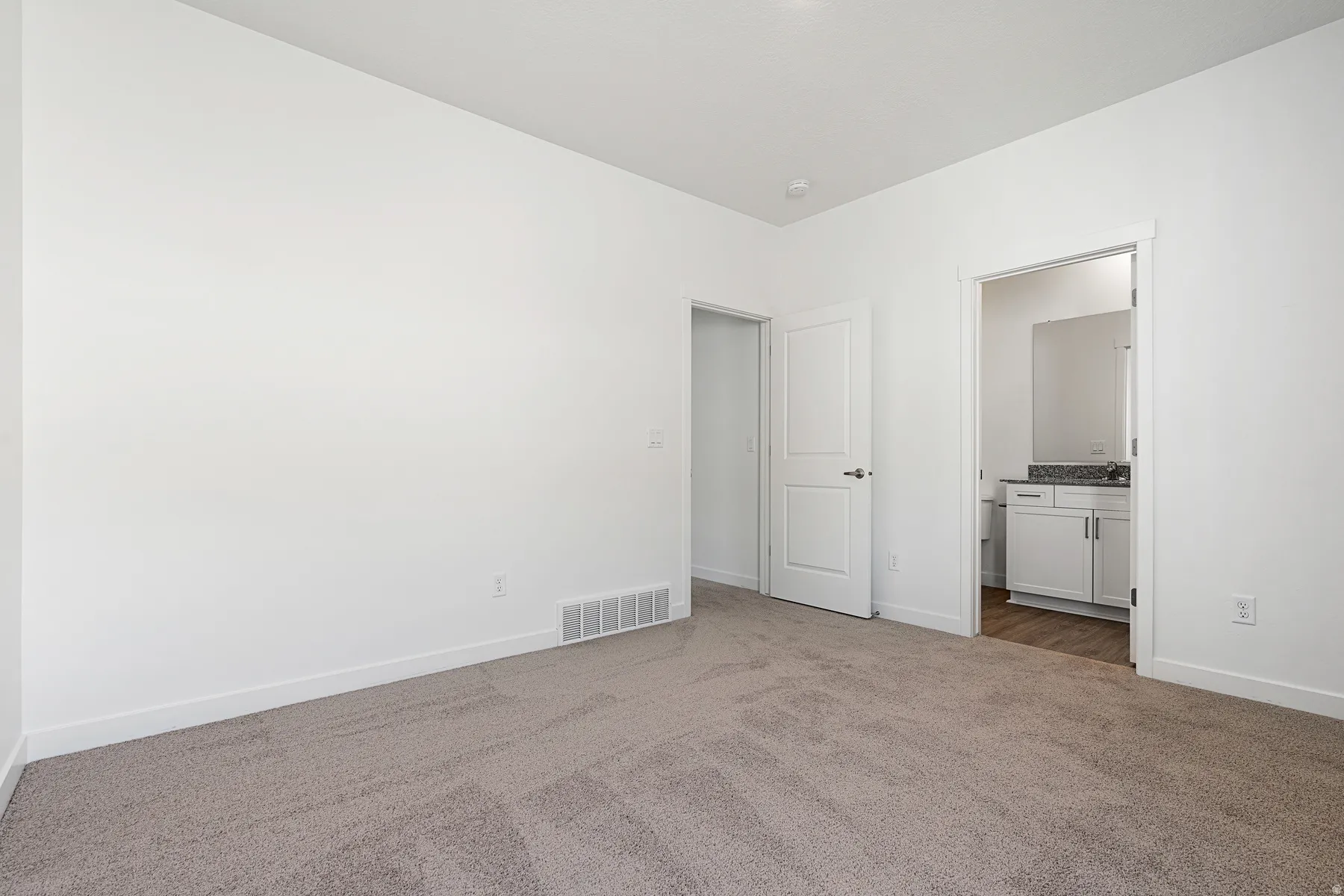 Unfurnished bedroom featuring dark carpet and connected bathroom
