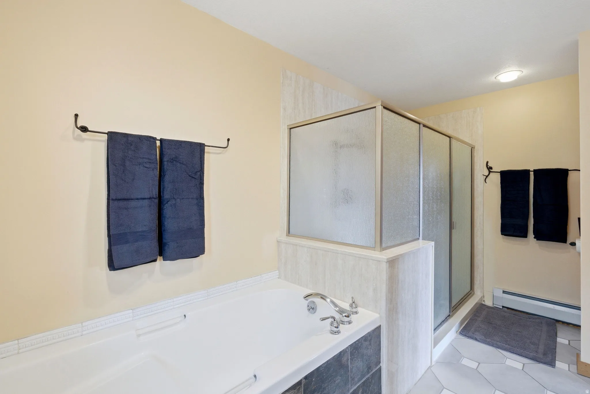 Bathroom featuring baseboard heating, a stall shower, a bath, and light tile patterned flooring