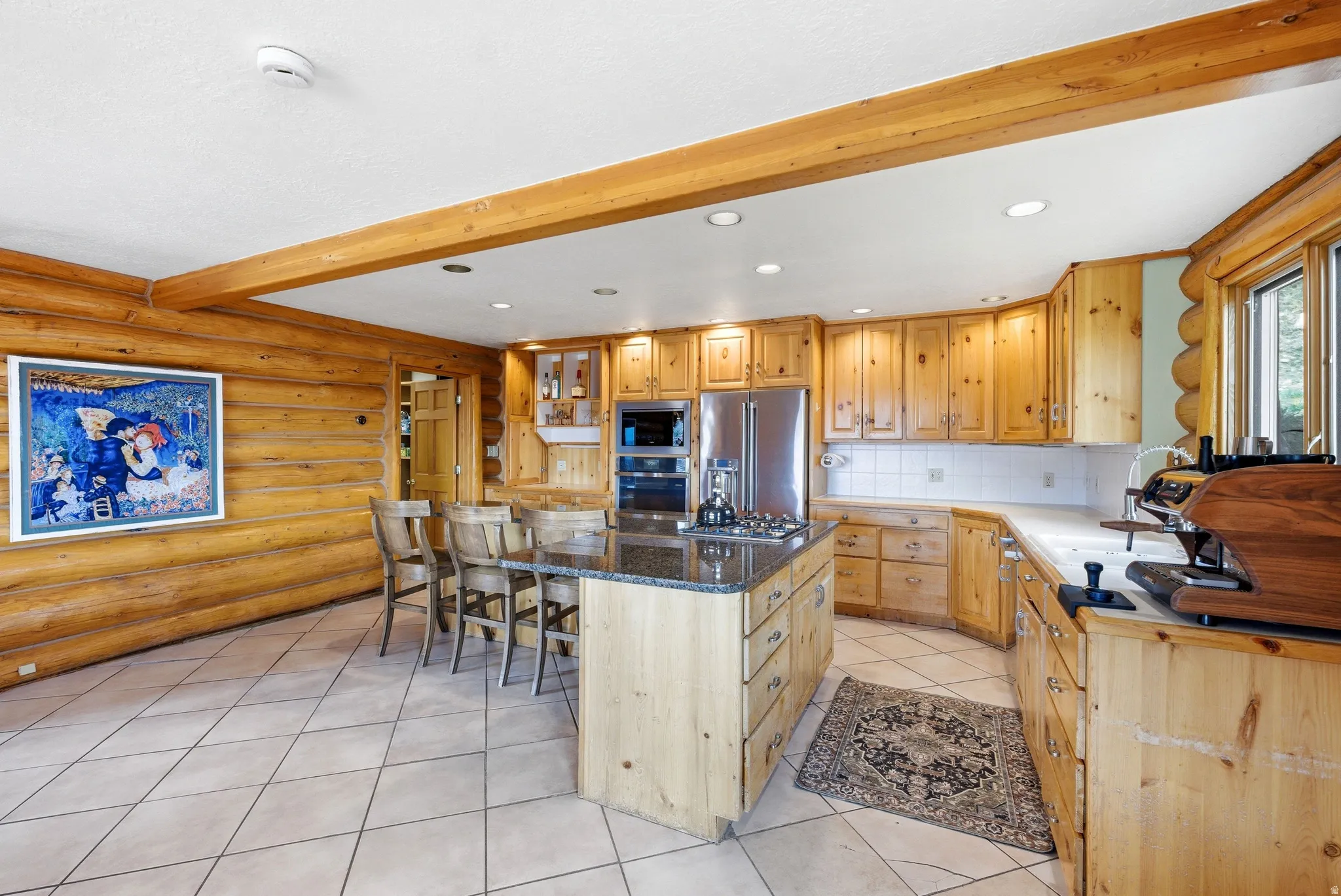 Kitchen with log walls, a center island, beam ceiling, light tile patterned flooring, and stainless steel appliances