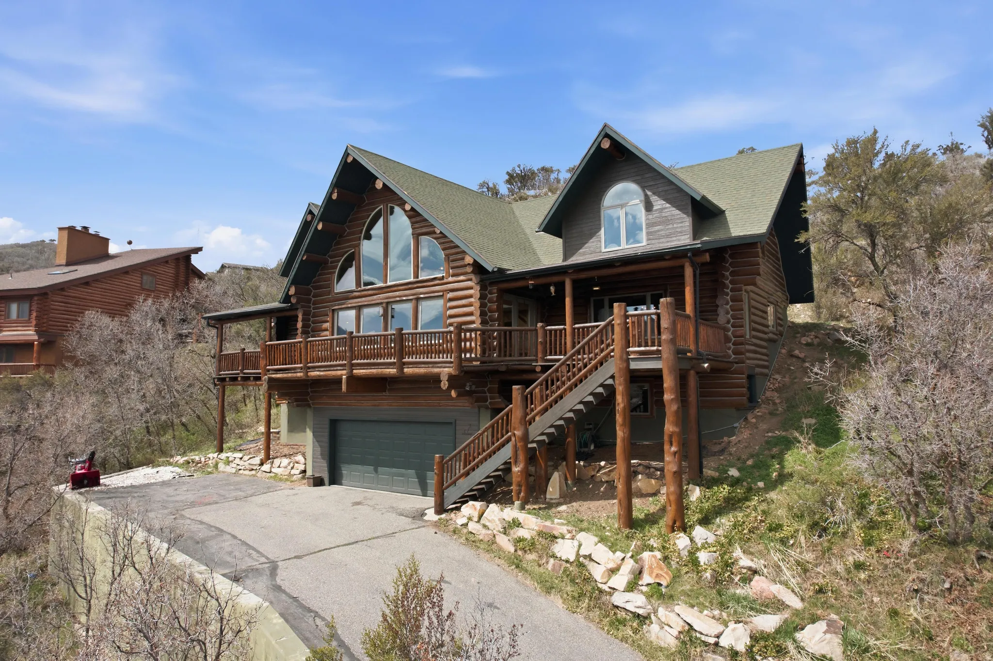 View of front of house with log exterior, a deck, a garage, driveway, and a shingled roof