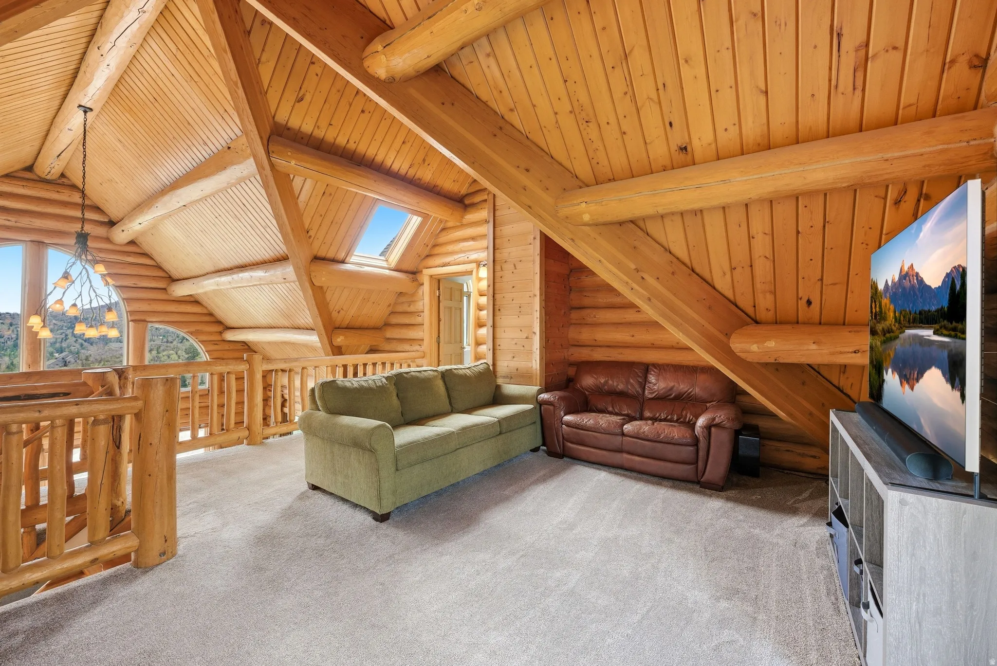 Carpeted living room with rustic walls, a skylight, vaulted ceiling with beams, and wooden ceiling