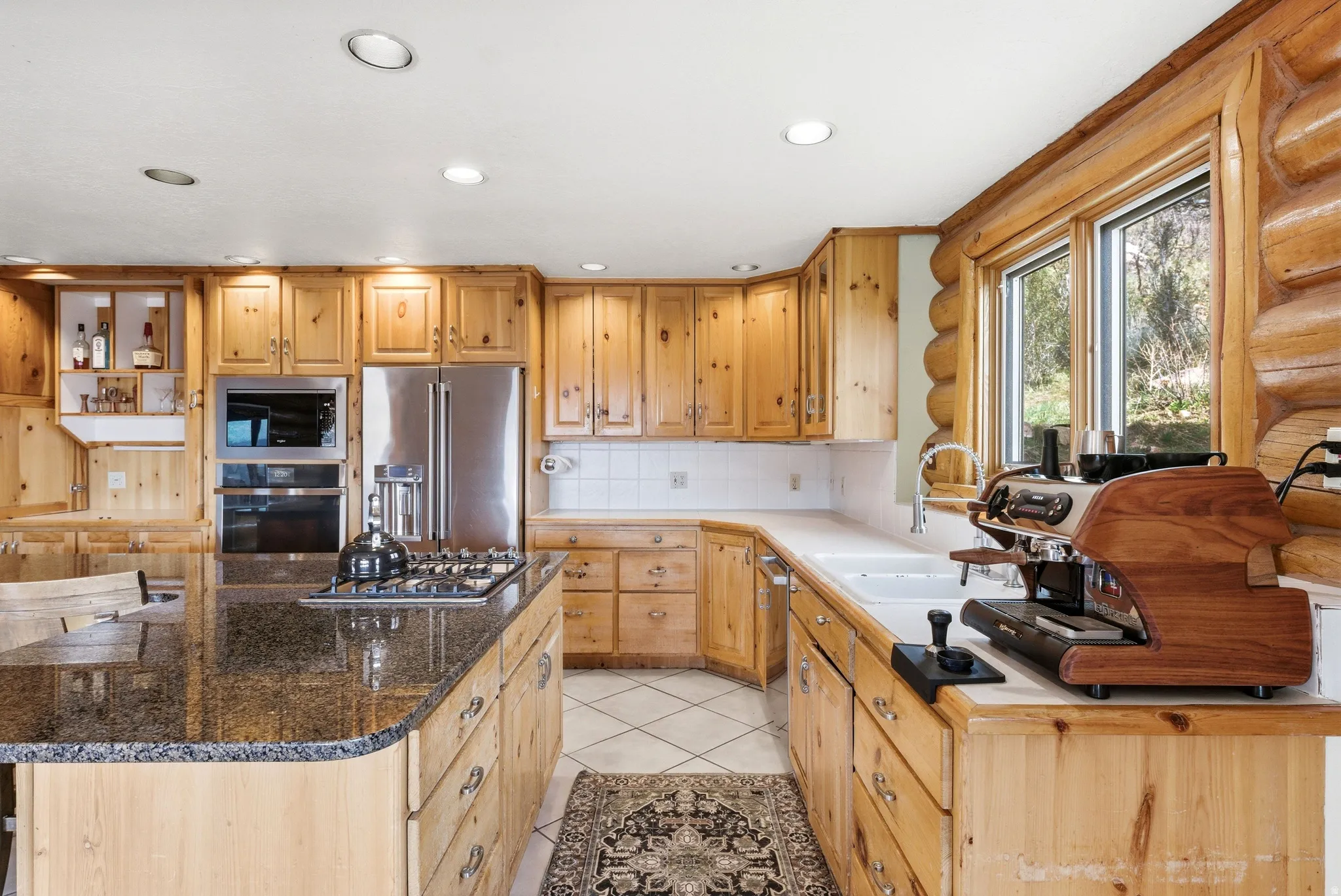 Kitchen with stainless steel appliances, a kitchen island, light tile patterned floors, light wood finish cabinets, and tasteful backsplash