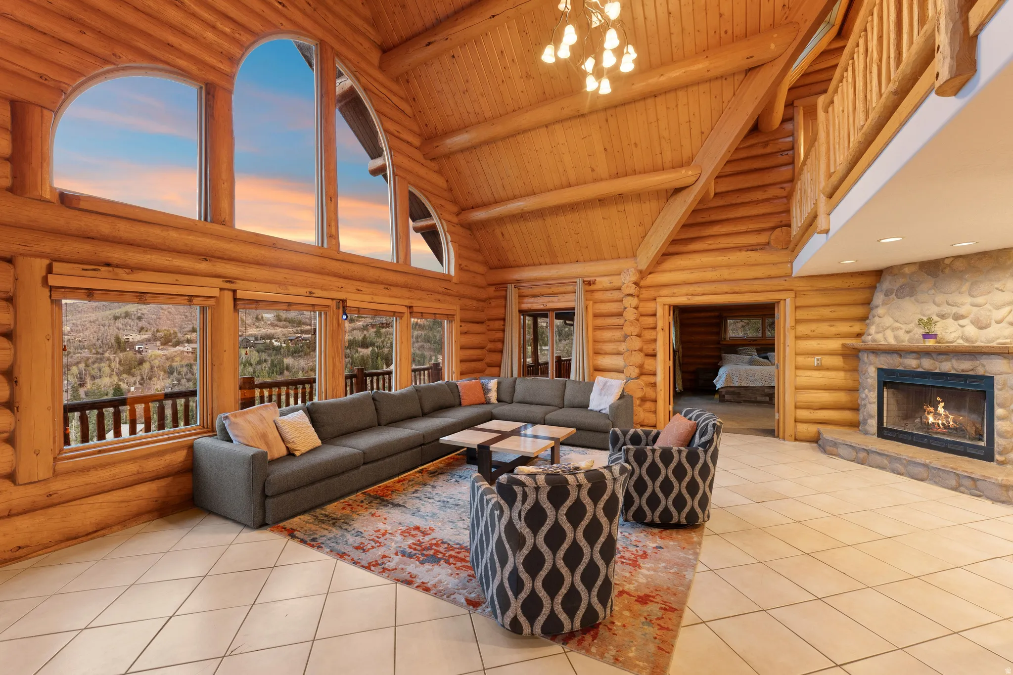 Living area with log walls, a chandelier, a fireplace, light tile patterned floors, and a high wooden beamed ceiling