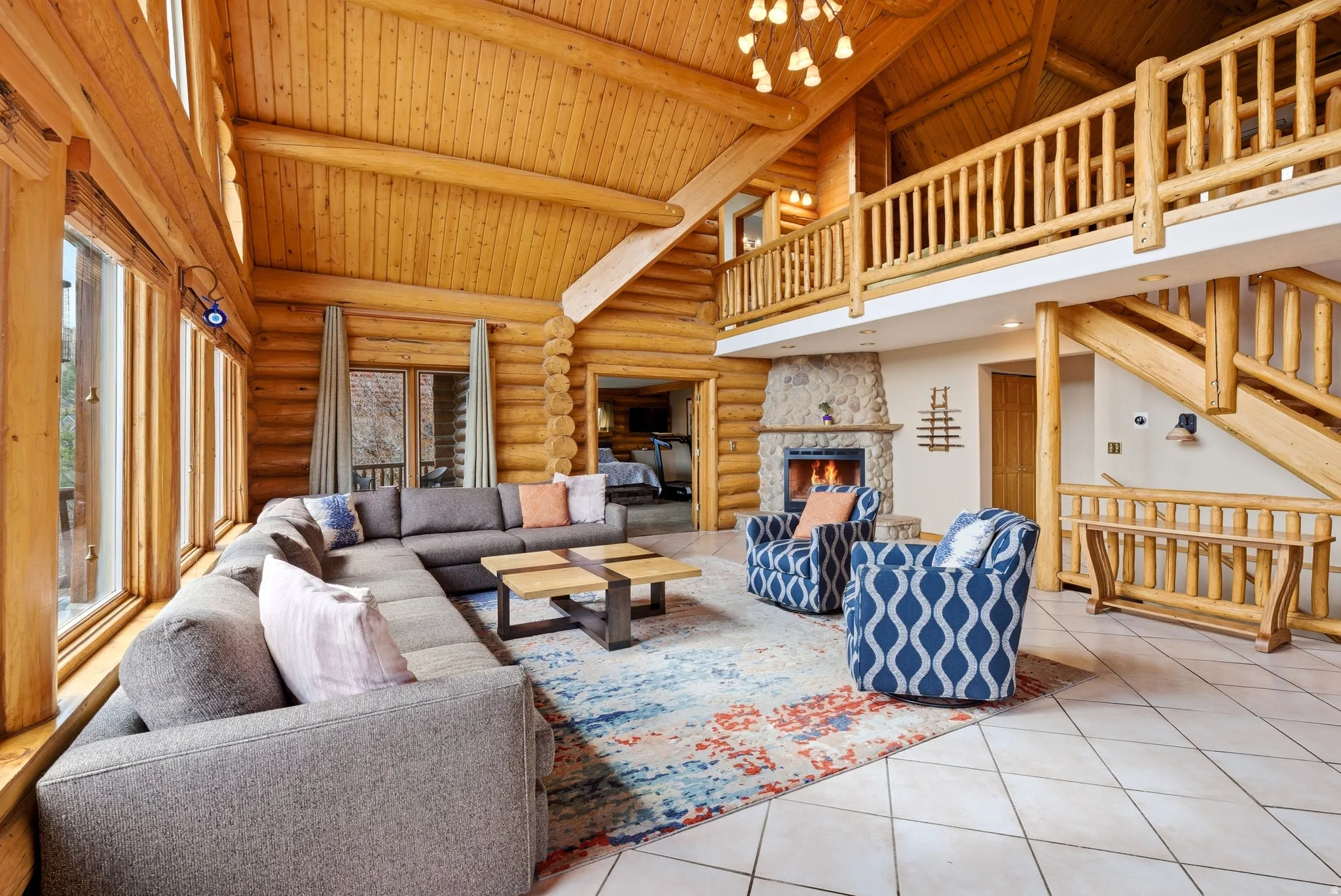 Living room with a stone fireplace, tile patterned flooring, log walls, a high wood beamed ceiling, and hanging lights