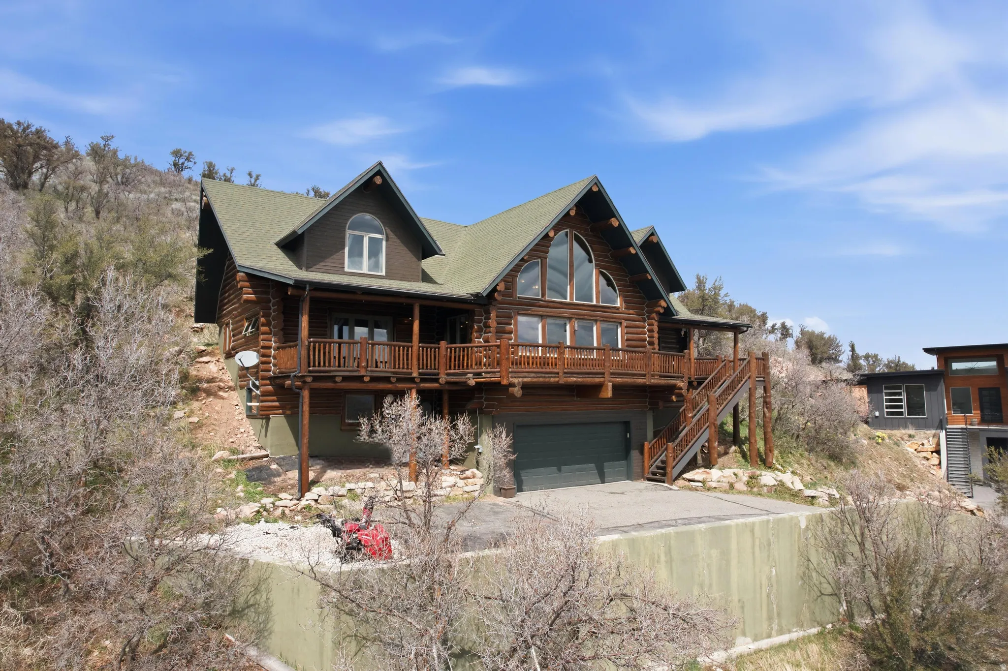 Log-style house featuring log siding, driveway, an attached garage, and a deck