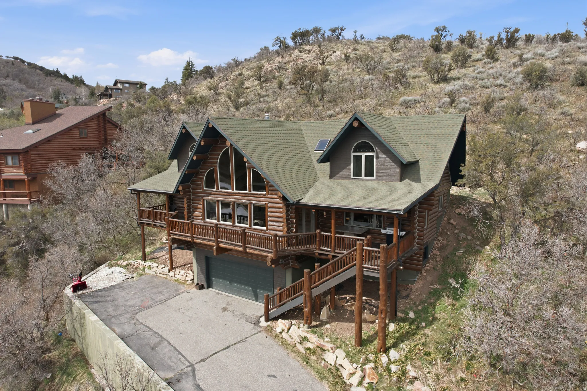 Log home with log siding, a deck with mountain view, a garage, roof with shingles, and asphalt driveway