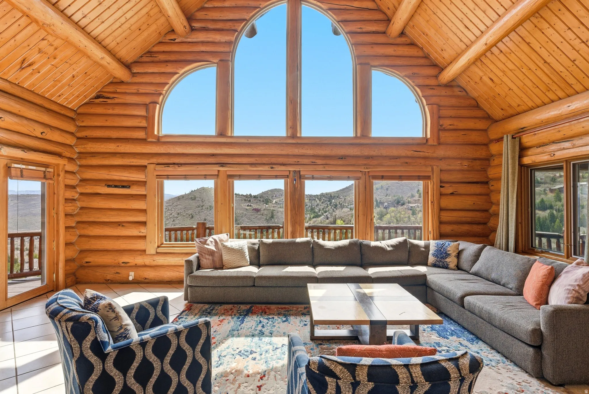 Tiled living area with a high wood beamed ceiling, log walls, and a mountain view