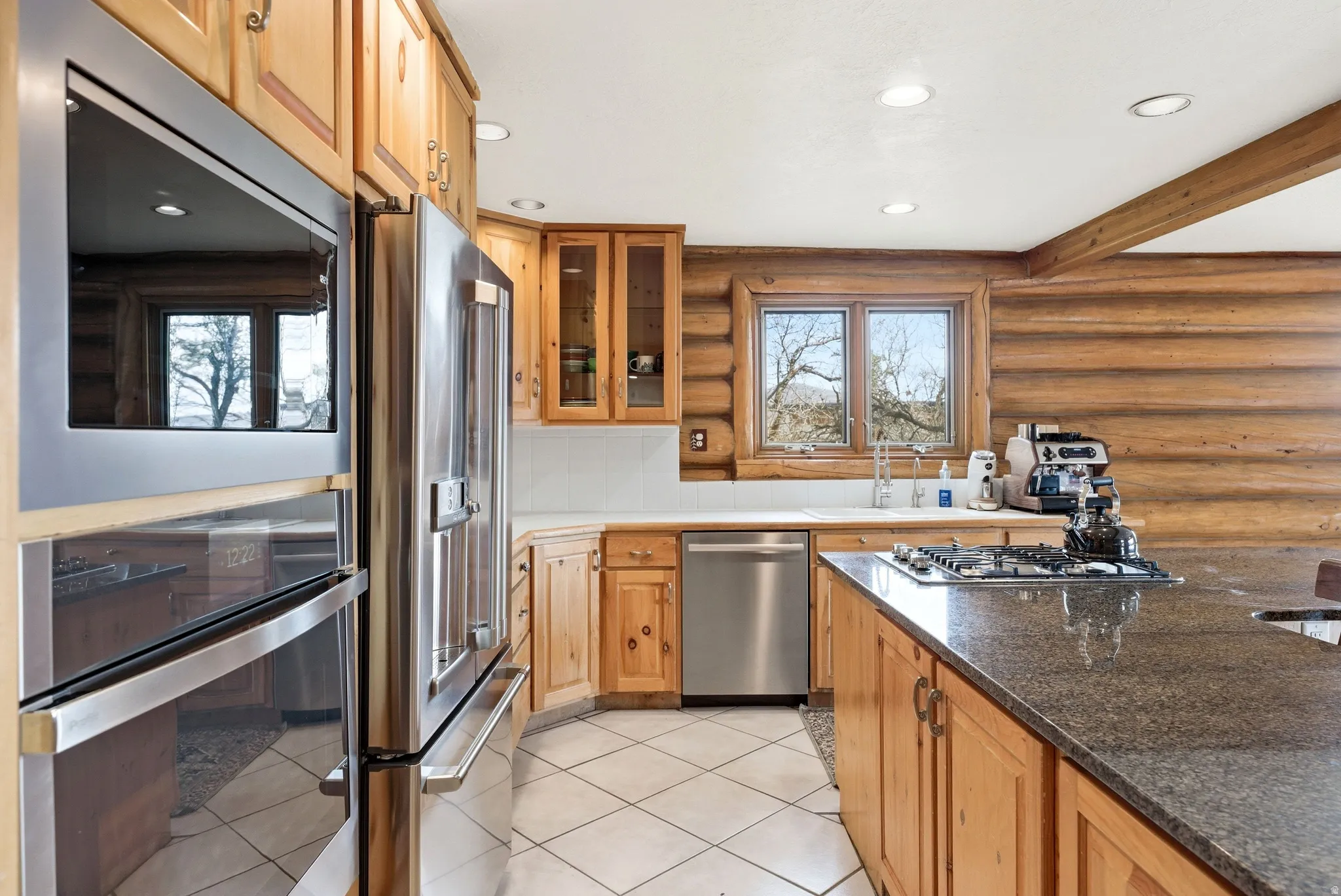 Kitchen featuring log walls, stainless steel appliances, recessed lighting, glass insert cabinets, and light tile patterned floors