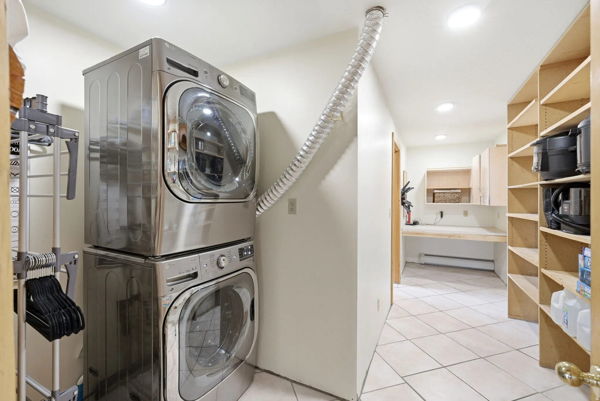 Laundry room featuring light tile patterned floors, stacked washer and dryer, recessed lighting, and a baseboard heating unit