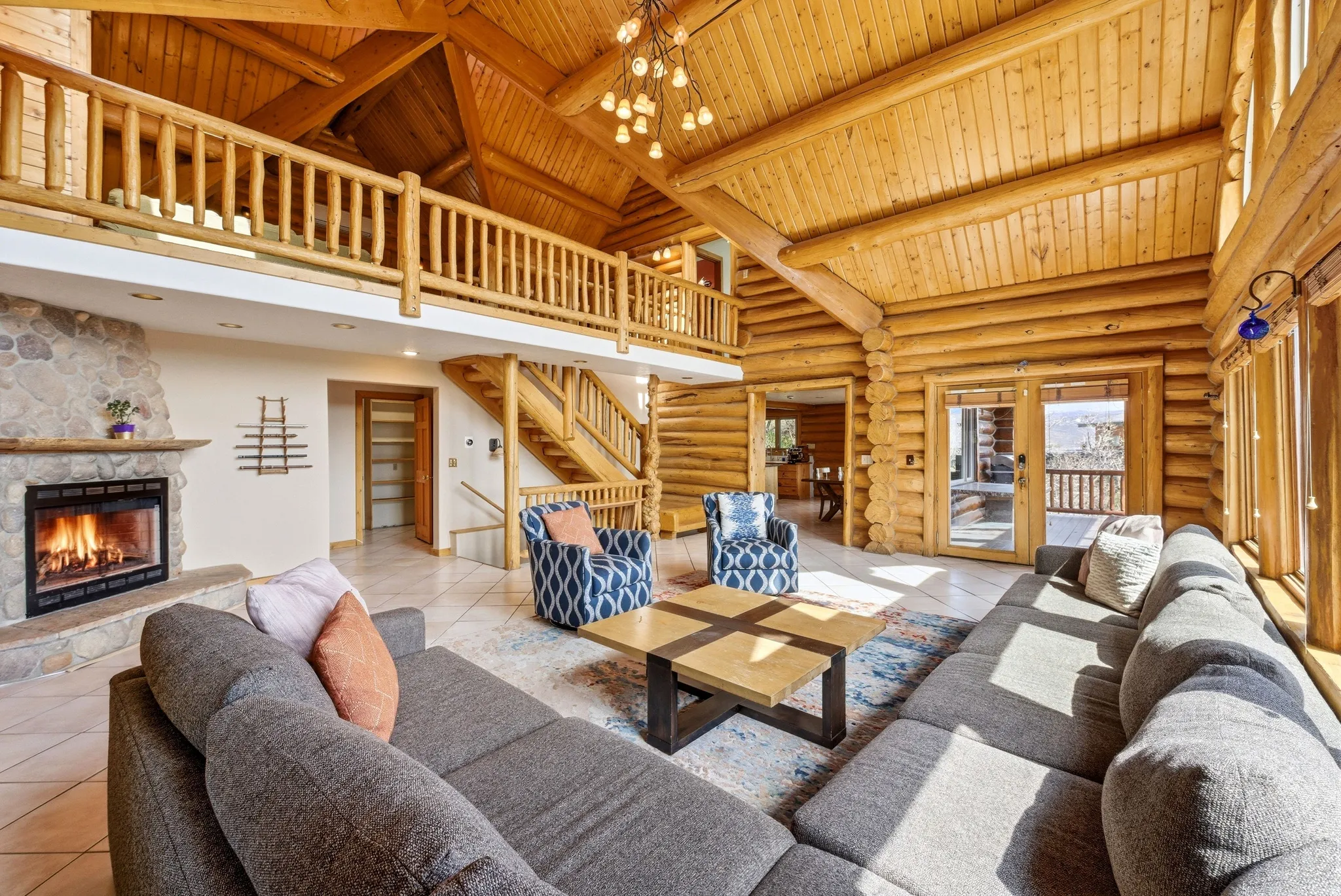 Living room with a high wood beamed ceiling, a fireplace, log walls, french doors, and a chandelier