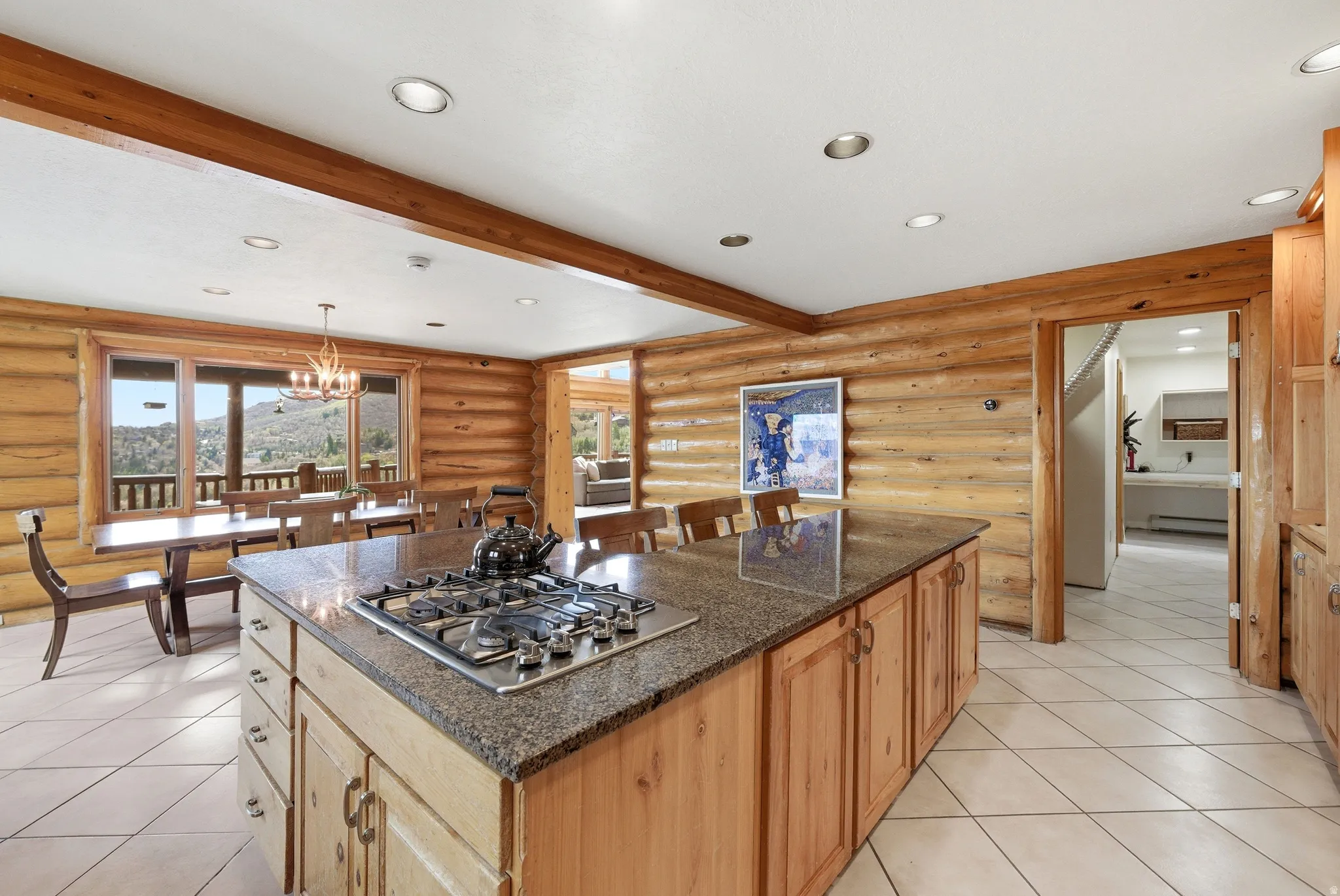 Kitchen featuring log walls, stainless steel gas cooktop, a center island, dark stone counters, and beam ceiling