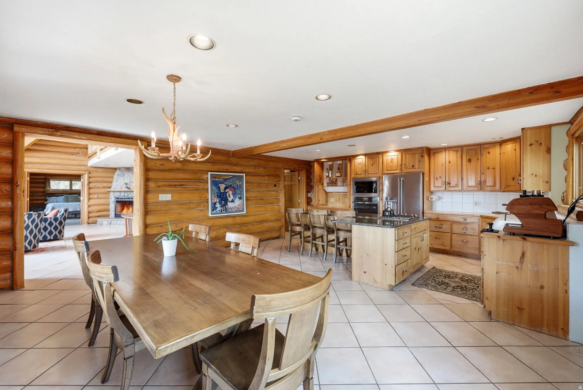 Dining room with log walls, a chandelier, light tile patterned flooring, and beam ceiling