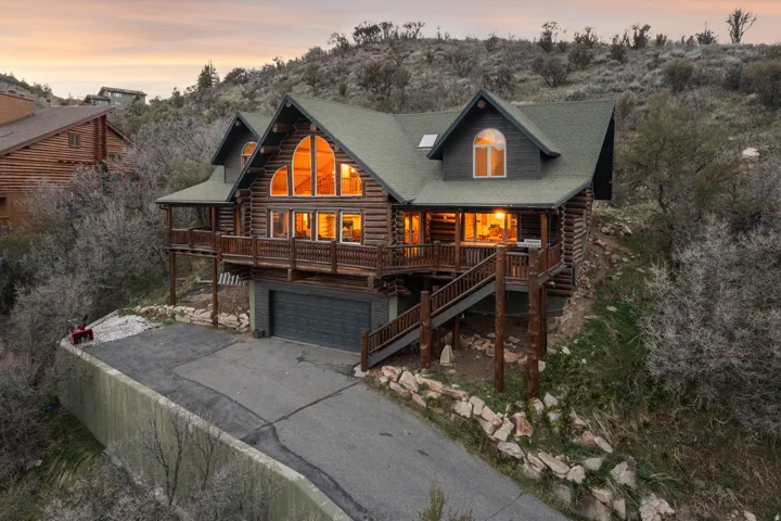 Cabin with log siding, an attached garage, asphalt driveway, and a deck