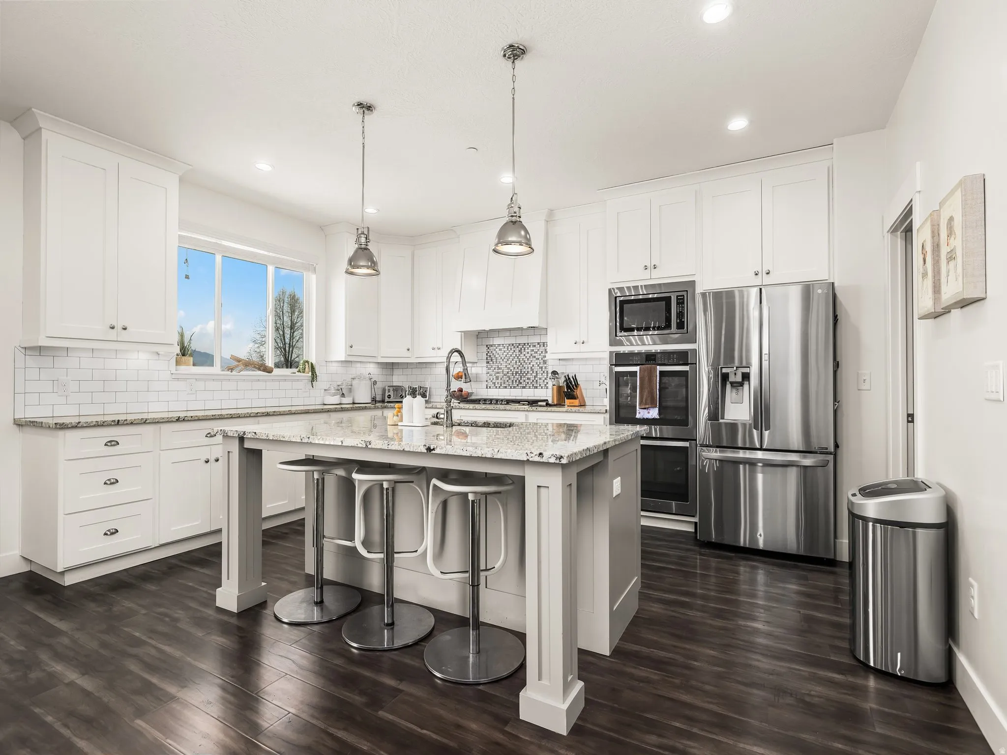 Kitchen featuring a breakfast bar area, stainless steel appliances, light stone countertops, decorative light fixtures, and a kitchen island with sink