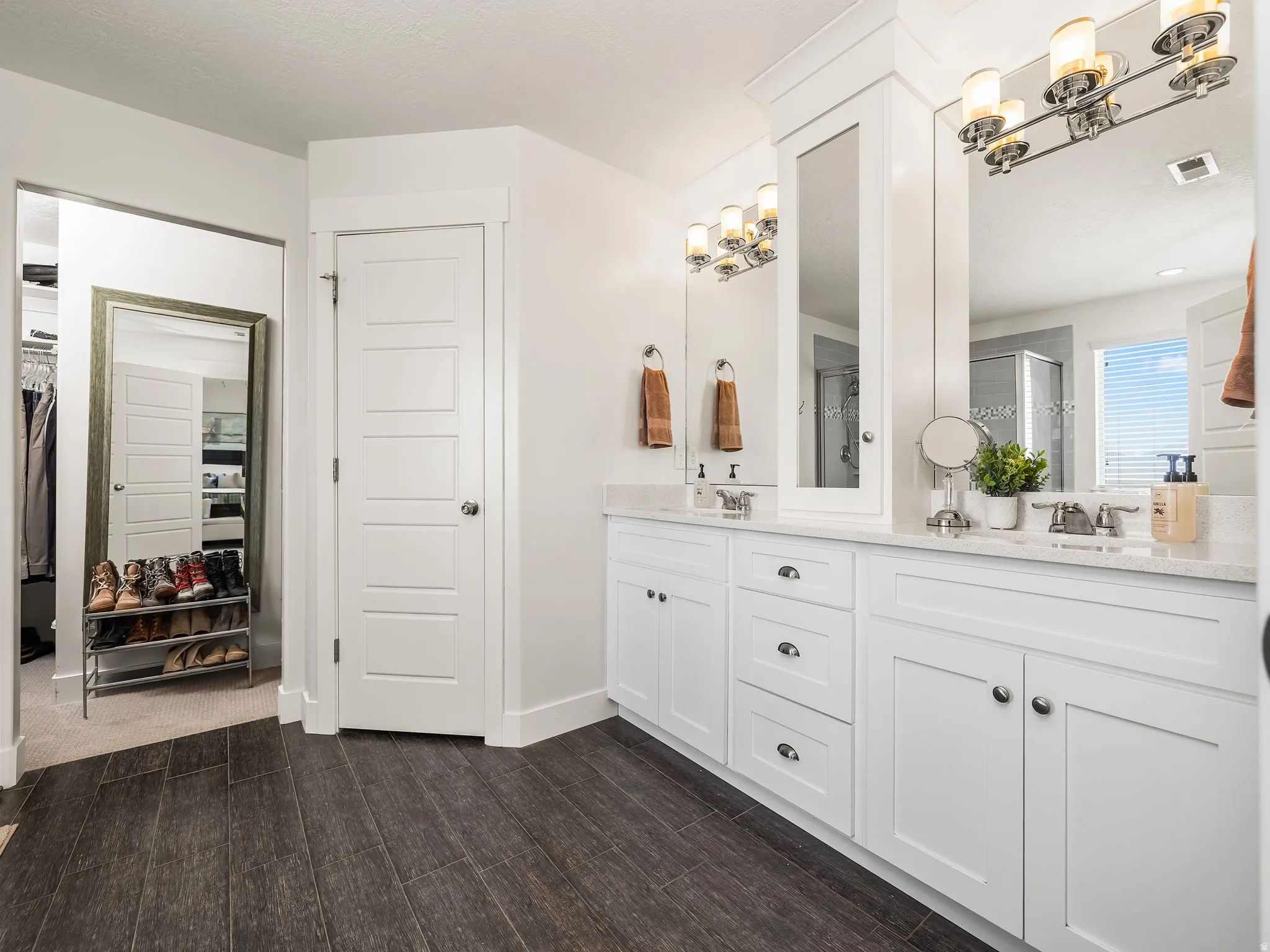 Full bath featuring a spacious closet, double vanity, a stall shower, and dark wood finished floors