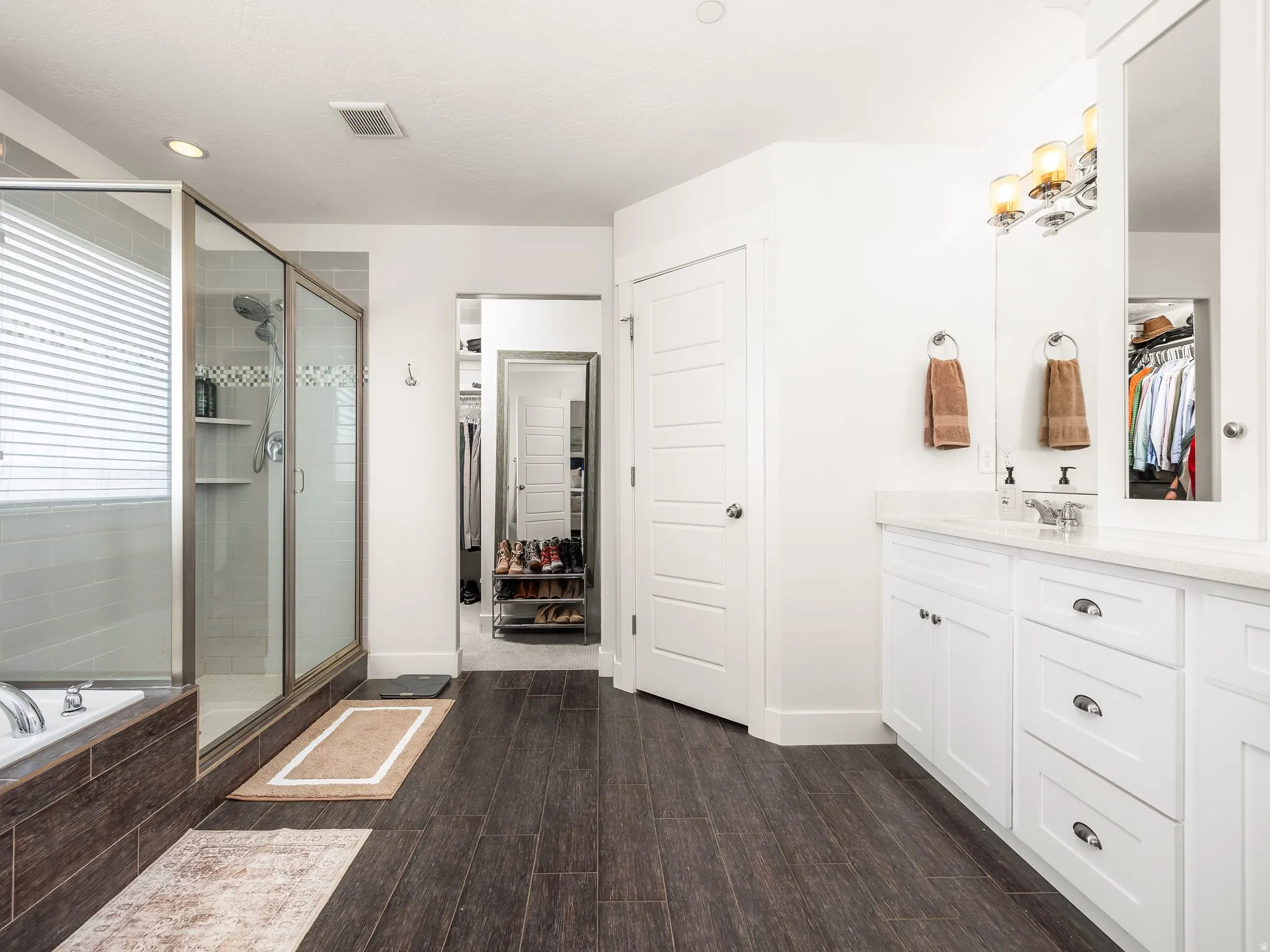 Full bathroom with a walk in closet, vanity, a shower stall, dark wood finished floors, and a bath