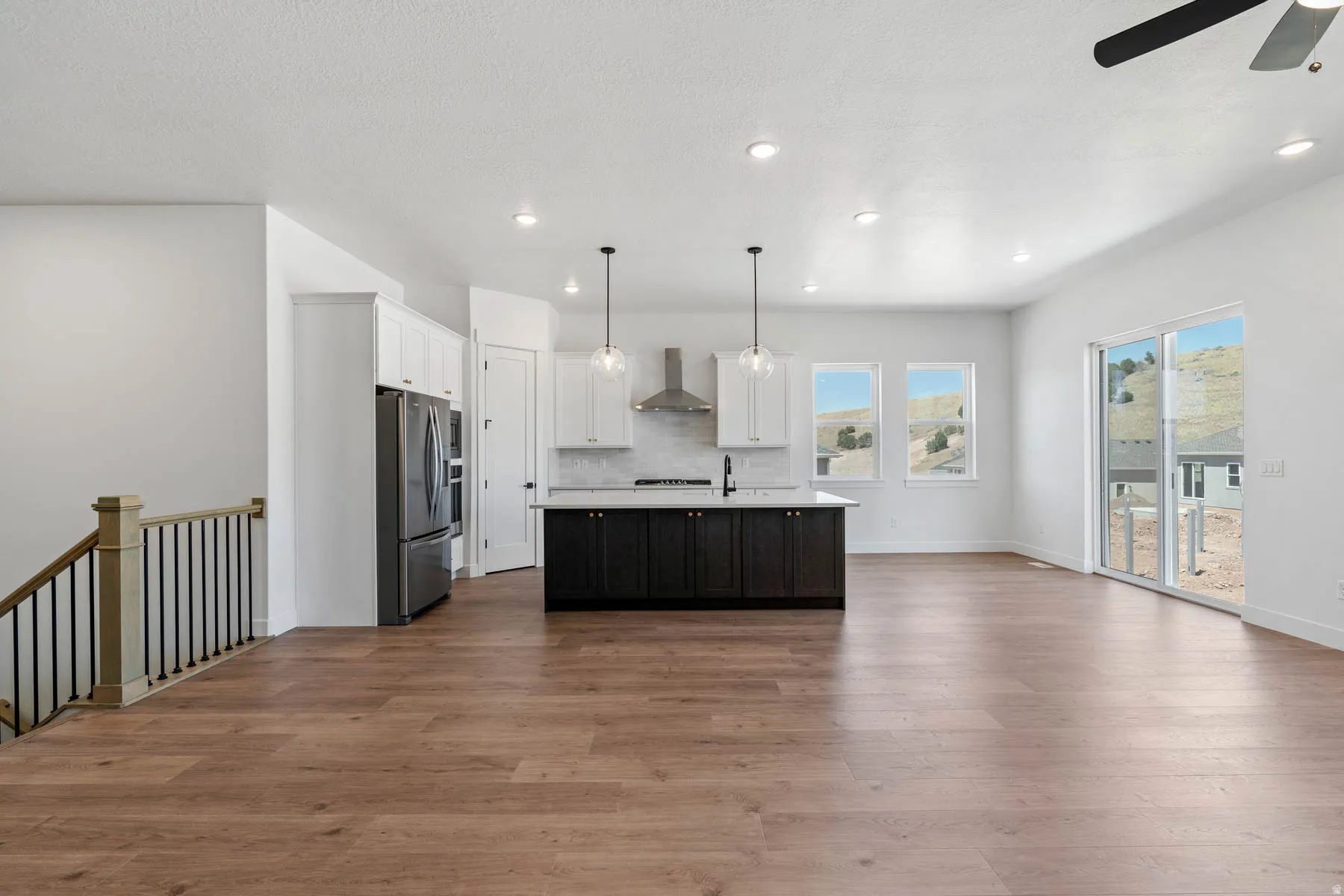 Dual tone kitchen featuring open floor plan, an island with sink, dual tone cabinetry, a ceiling fan, and decorative light fixtures