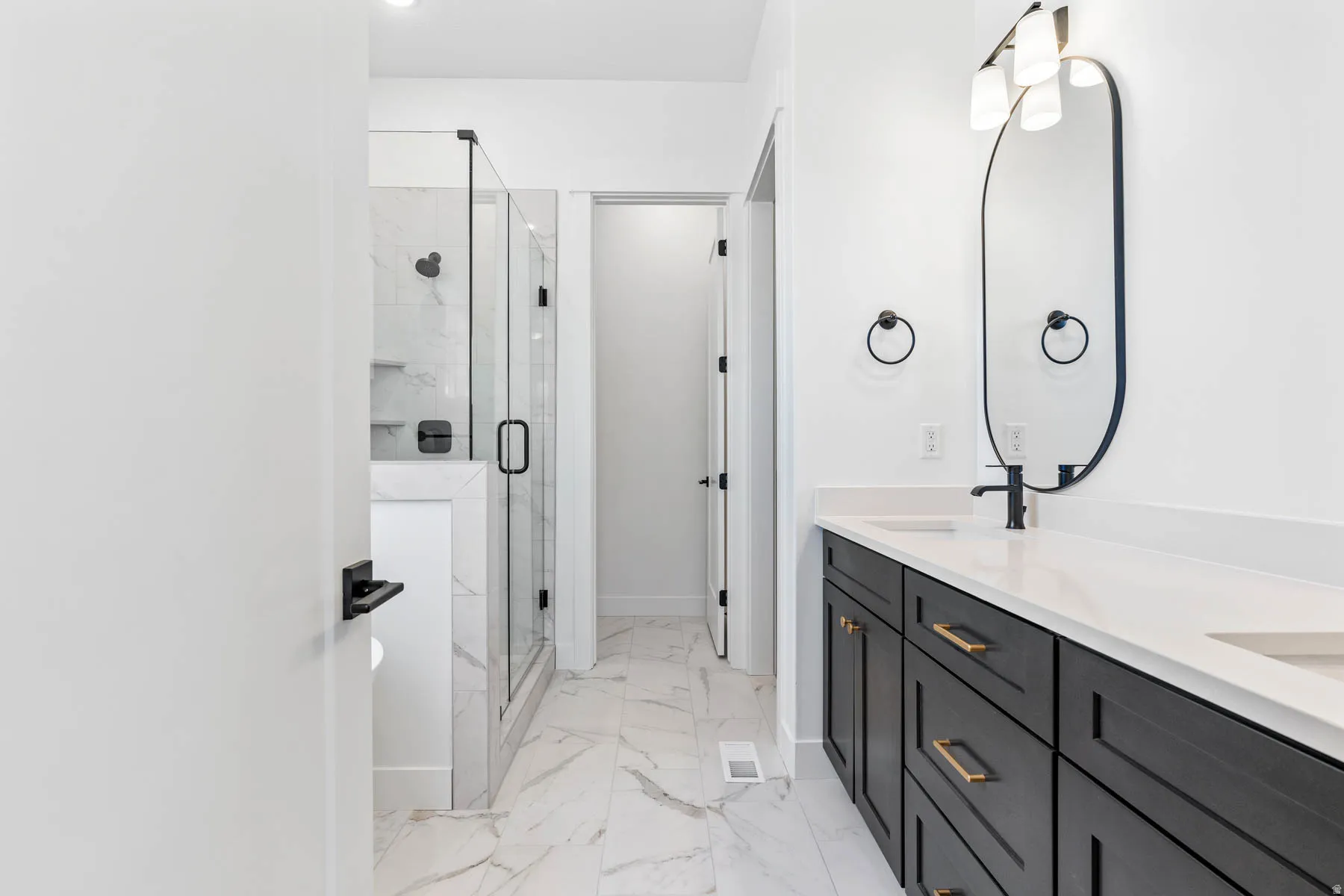 Full bathroom featuring double vanity, a marble finish shower, and light marble finish floors