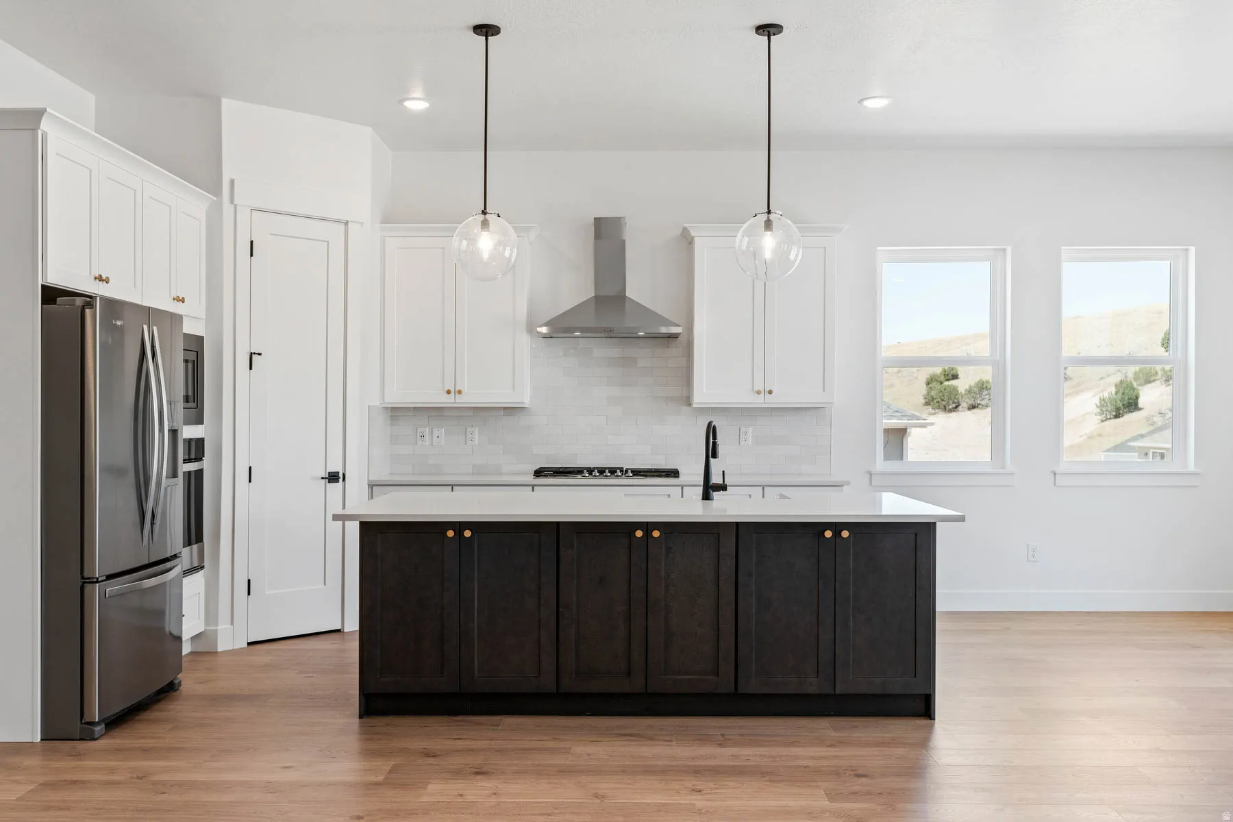 Two tone kitchen with stainless steel appliances, dual tone cabinetry, decorative light fixtures, a kitchen island with sink, and light wood finished floors
