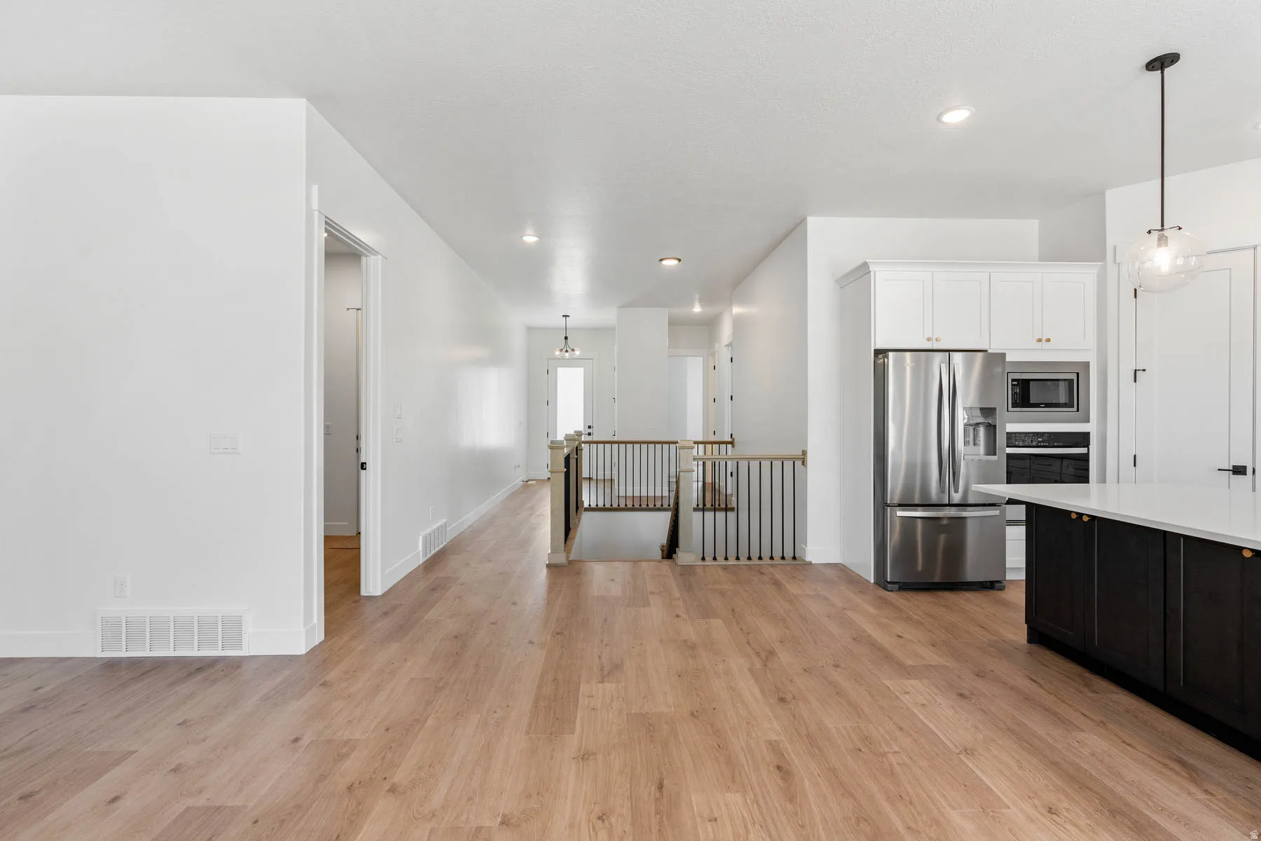 Two tone kitchen featuring stainless steel appliances, pendant lighting, two tone cabinets, and light wood finished floors