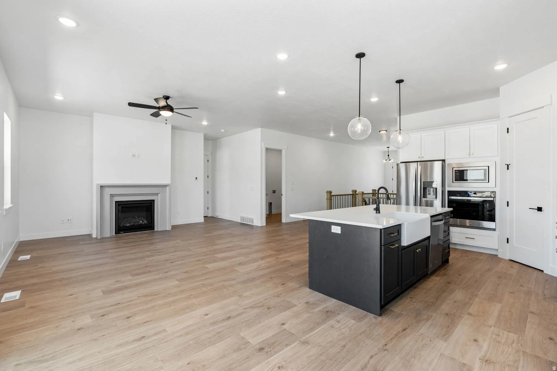 Two tone kitchen with an island with sink, open floor plan, hanging light fixtures, two tone color scheme, and stainless steel appliances