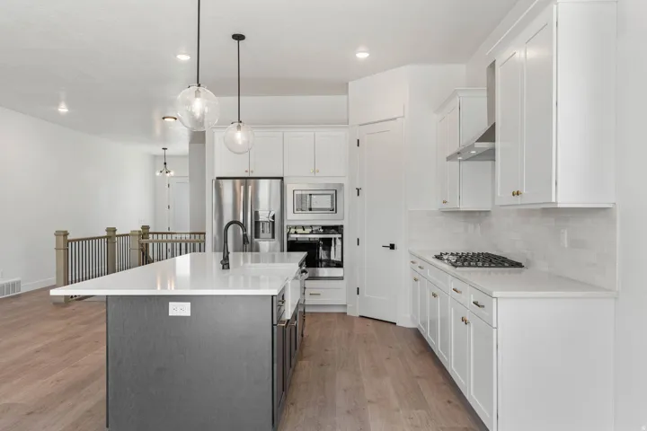 Two tone kitchen with two tone cabinets, stainless steel appliances, a kitchen island with sink, light wood-type flooring, and pendant lighting