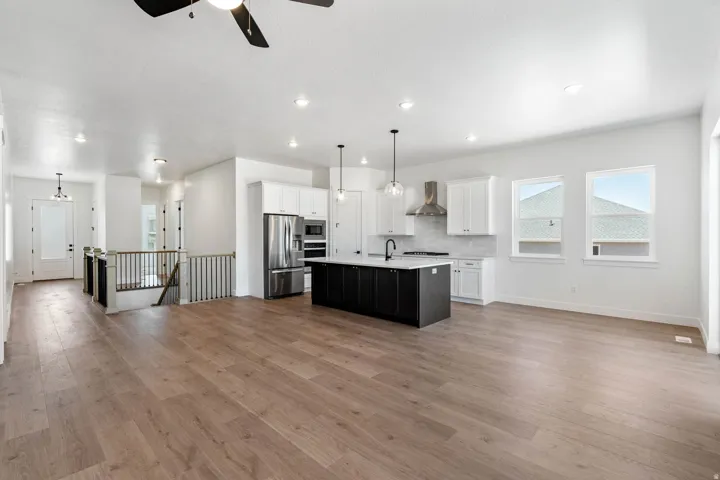 Dual tone kitchen featuring open floor plan, stainless steel appliances, hanging light fixtures, an island with sink, and a ceiling fan