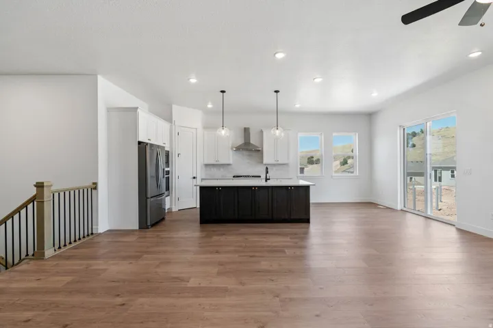 Dual tone kitchen featuring open floor plan, an island with sink, dual tone cabinetry, a ceiling fan, and decorative light fixtures