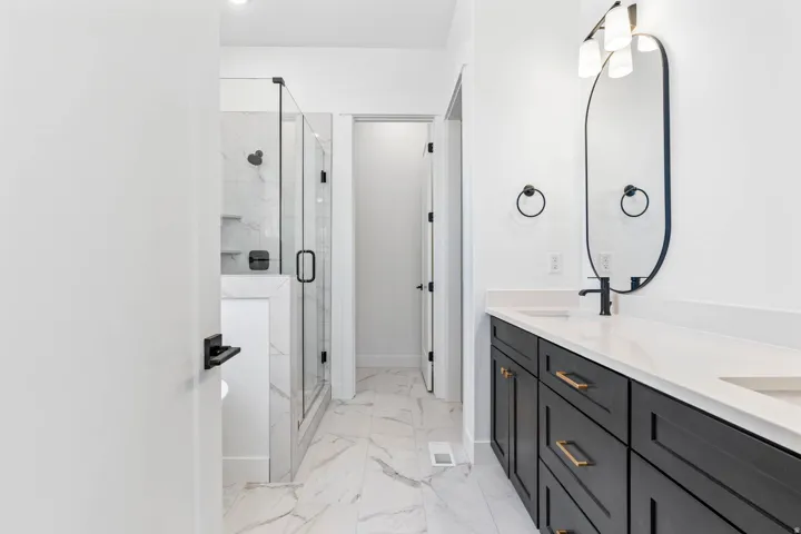 Full bathroom featuring double vanity, a marble finish shower, and light marble finish floors