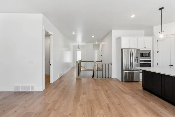 Two tone kitchen featuring stainless steel appliances, pendant lighting, two tone cabinets, and light wood finished floors