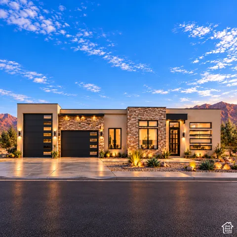 Modern exterior featuring a stucco finish, stacked stone accents, multi-panel garage doors with horizontal glass insets, large picture windows, and xeriscaped front grounds