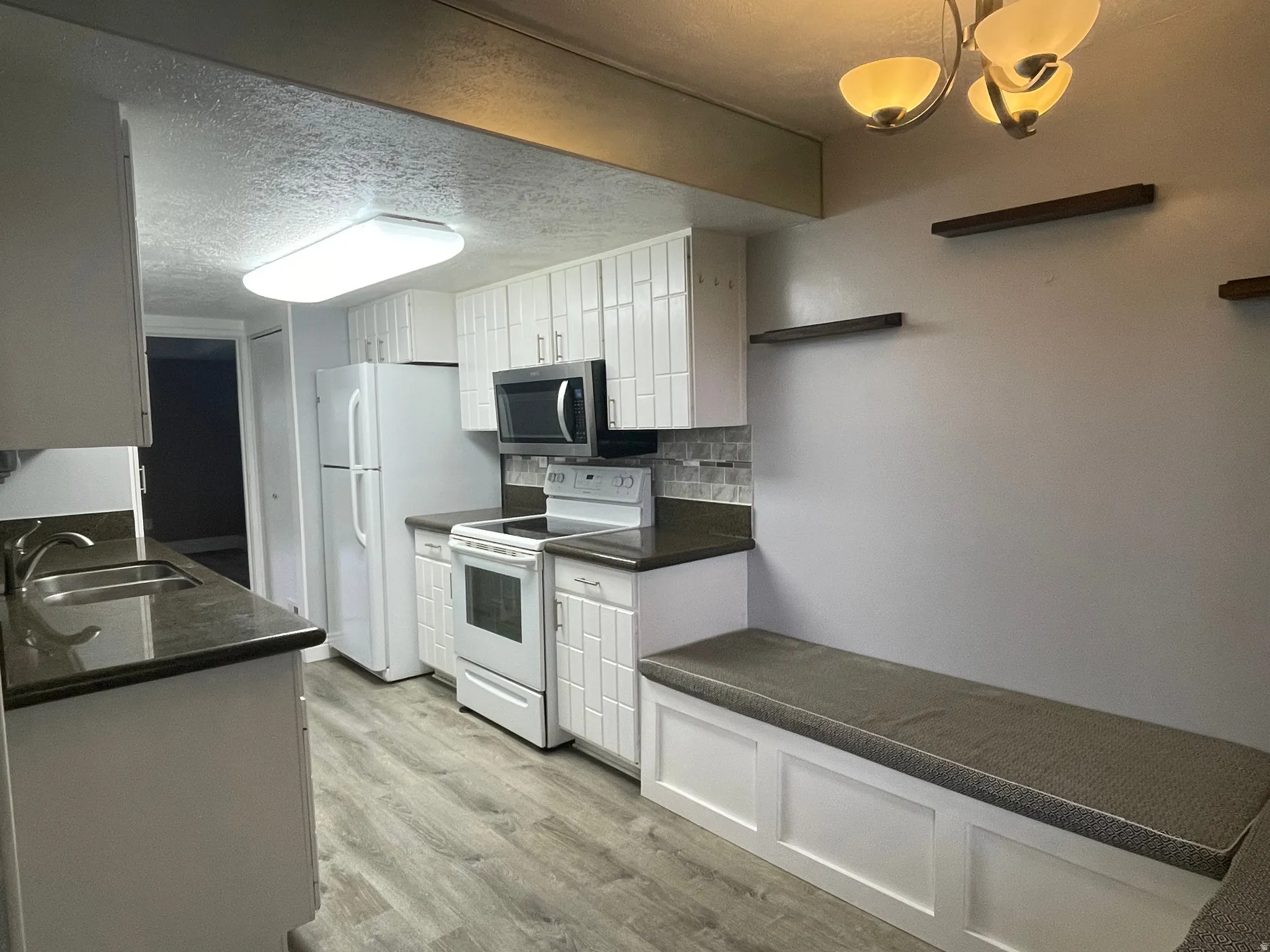 Updated kitchen featuring white cabinetry, cushioned storage bench, white electric range oven, light wood-style floors, backsplash, and a textured ceiling