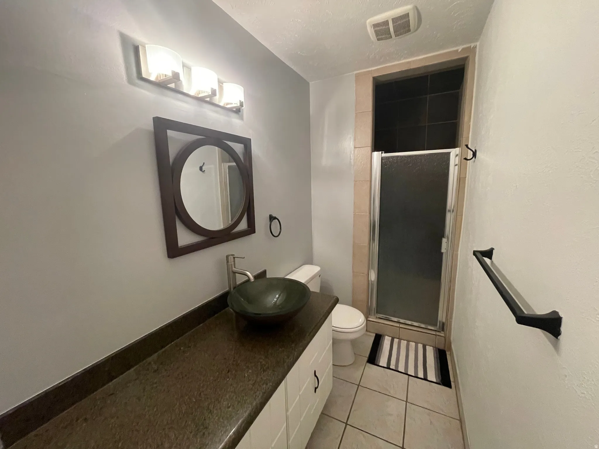 Hallway Bathroom featuring a tiled stall shower, vanity, light tile patterned floors, and a textured ceiling